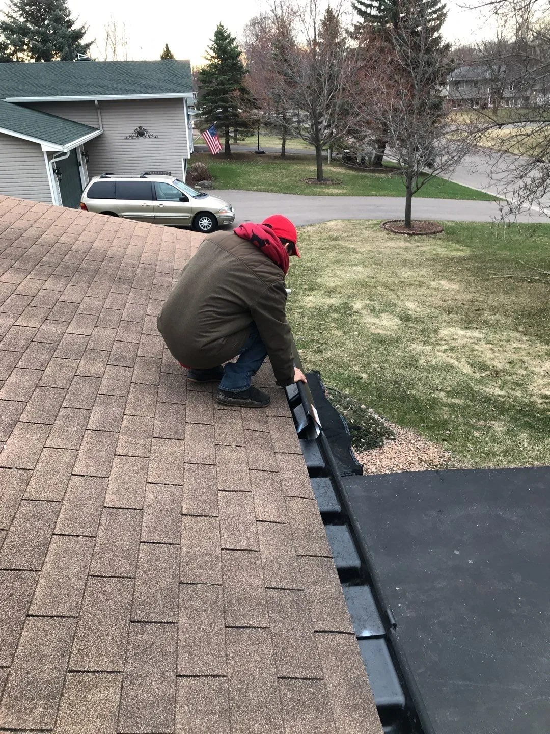 A roofer working with a gutter protection piece beside a shingle roof