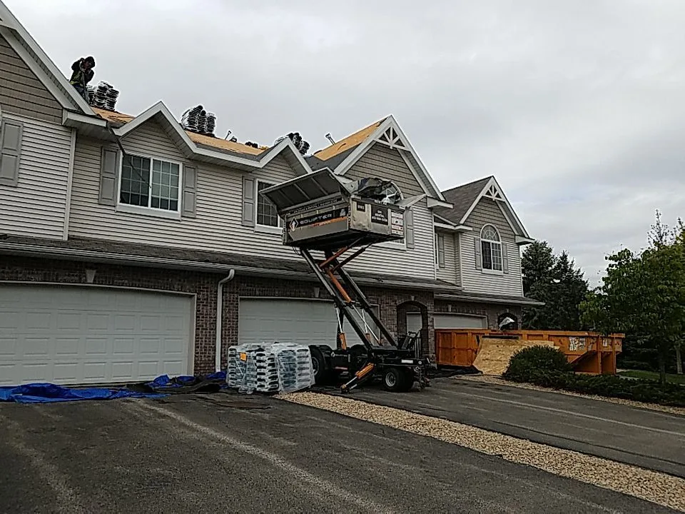 Shingle roofs on a row of townhomes with roofing equipment alongside